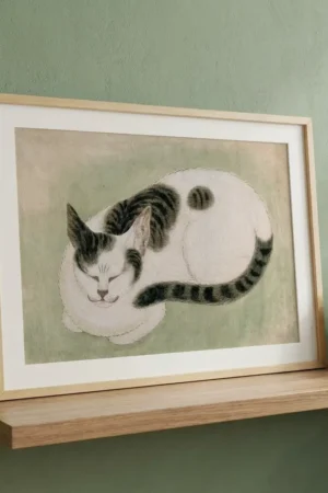 Framed illustration of a sleeping white cat with black markings on a wooden shelf against a green wall.