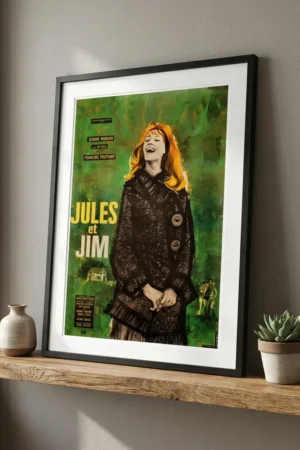 Framed green Jules et Jim poster on a wooden shelf beside a small vase and a succulent plant.