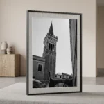 Framed black and white printable art of the Campanile dei Cappuccini bell tower in Taormina, Sicily—a dramatic upward view between stone arches, captured by Mark Marsh and displayed in a modern interior.