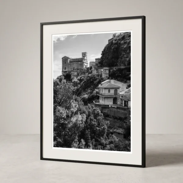 Church of San Nicolò black and white printable art by Mark Marsh in Frame Framed black and white printable art of Chiesa di San Nicolò in Savoca, Sicily—viewed across a steep valley with Mediterranean trees and tiled roofs below the crowning church, captured by Mark Marsh and displayed in a modern interior.