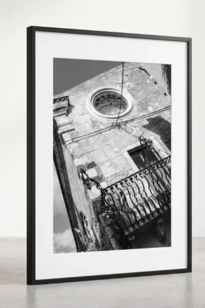 Framed Taormina Corso Umberto black and white digital wall art print by Mark Marsh, showing the round glass clock window and ornate wrought-iron balcony detail.