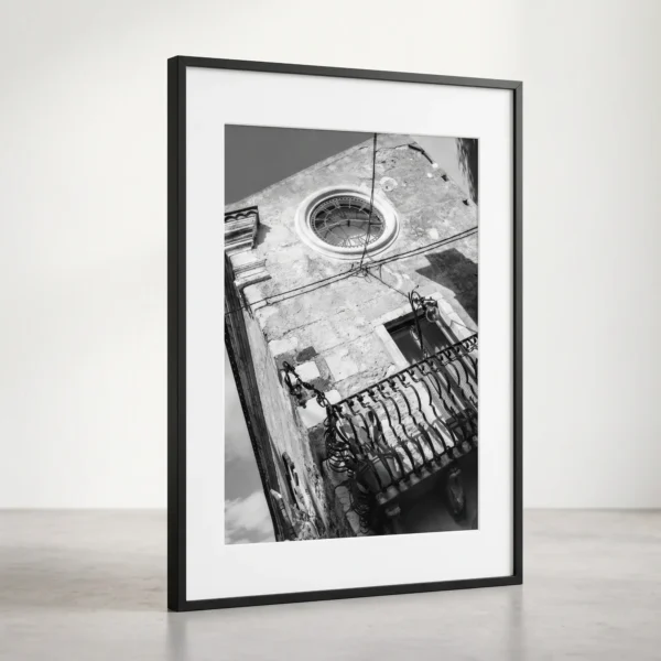 Clock window on Corso Umberto digital printable art in black frame and on marble floor by Mark Marsh Framed Taormina Corso Umberto black and white digital wall art print by Mark Marsh, showing the round glass clock window and ornate wrought-iron balcony detail.