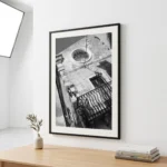 Framed black and white printable art of a historic clock facade on Corso Umberto I in Taormina, Sicily—round clock window, wrought-iron balcony, and stone wall, captured by Mark Marsh and displayed in a modern interior.