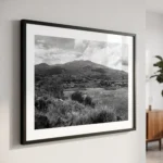 Framed black and white printable art of Mount Etna rising from raw volcanic foothills in Sicily—basaltic lava stone, wild scrub, and cloud cover, captured by Mark Marsh and displayed in a modern interior.