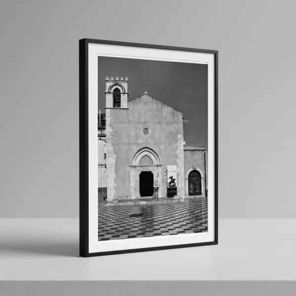 Former Church of Sant'Agostino print by Mark Marsh on bench Sant'Agostino Taormina black and white digital download print in a black frame, styled on a shelf with stone textures, capturing Sicilian Gothic architecture by Mark Marsh.