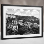 Framed black and white printable art of Savoca, the Godfather village in Sicily—terraced stone houses, white apartments, and forested ridges beneath a cloud-filled sky, captured by Mark Marsh.