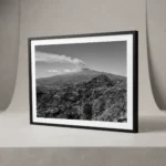 Framed black and white printable art of Mount Etna venting smoke across a wide Sicilian panorama, viewed from Taormina—layered ridges and hillside villages below, captured by Mark Marsh.