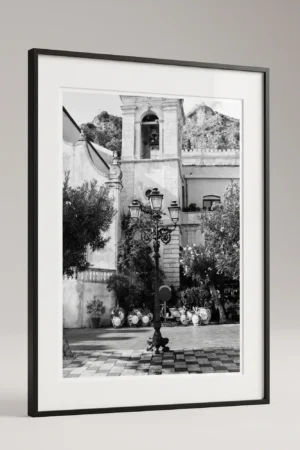 Framed Taormina piazza black and white digital wall art print by Mark Marsh, showing the cast-iron lamppost, decorative brackets, and checkerboard tile floor detail.