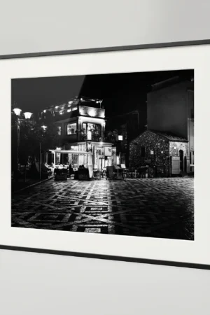 , styled in a bedroom or living room with warm wood and stone textures, capturing Sicilian village night by Mark Marsh. Keywords for SEO Primary: Castelmola printable art, Sicily black and white print, Piazza Sant'Antonino, digital wall art Sicily, Italian village print, monochrome nocturne print, Sicily digital download Secondary: Antico Caffè San Giorgio, Piazza Belvedere, Sicilian village night, mosaic floor art, Mediterranean piazza print, atmospheric travel art Long-tail: black and white print of Castelmola piazza, Piazza Sant'Antonino night photo, printable Italian village wall art, monochrome Sicilian nocturne photography, Castelmola piazza print download Brand: Mark Marsh, Neurodecorating, The Art of Digital Living, Sicily in Black & White collection.