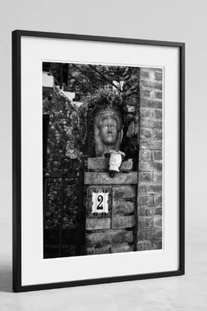 Framed Taormina Testa di Moro black and white digital wall art print by Mark Marsh, showing the sculpted ceramic face, trailing plant leaves, and rose-bordered house number tile detail.
