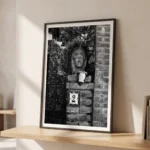 Framed black and white printable art of a Sicilian Testa di Moro ceramic planter on a residential gate in Taormina—sculpted head with trailing foliage above a house number tile, captured by Mark Marsh and displayed in a modern interior.