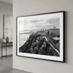 Framed black and white printable art of San Domenico Palace in Taormina, Sicily—perched on a clifftop promontory above the Ionian Sea with a forested ravine in the foreground, captured by Mark Marsh and displayed in a modern interior.