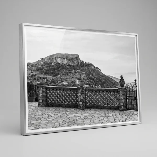 Scenic view looking out from Castelmola printable art by Mark Marsh in large grey frame Framed black and white printable art of Monte Veneretta viewed from a stone terrace in Castelmola, Sicily—woven brick balustrade, ceramic planters, and limestone peak beyond, captured by Mark Marsh.