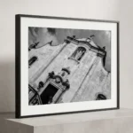 Framed black and white printable art of Chiesa di San Giuseppe in Taormina, Sicily—canted vertical view of the Baroque facade with Christ the King statue in an alcove, captured by Mark Marsh and displayed in a modern interior.