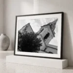 Framed black and white printable art of the San Giuseppe bell tower above Piazza IX Aprile in Taormina, Sicily—canted low-angle view of the Baroque campanile and spire, captured by Mark Marsh and displayed in a modern interior.