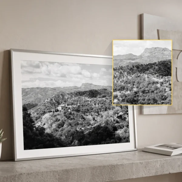 Framed black and white printable art of a solitary stone farmhouse in the Peloritani mountains near Savoca, Sicily—wild Mediterranean macchia, olive groves, and layered ridges, captured by Mark Marsh and displayed in a modern interior.