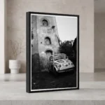 Framed black and white printable art of a classic white Fiat 500 parked on a steep stone street in Castelmola, Sicily—captured by Mark Marsh and displayed in a modern interior.