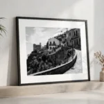 Savoca Sicily black and white digital download print in a black frame, styled on a shelf with a plant and vase, capturing the cinematic Godfather filming location by Mark Marsh.