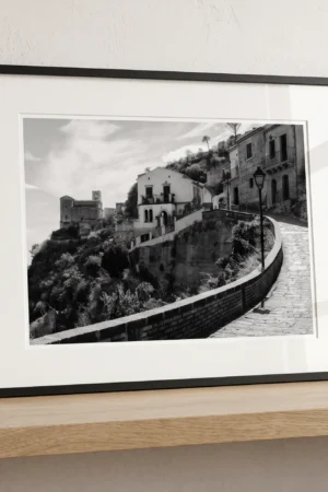 Framed Savoca Sicily black and white digital wall art print by Mark Marsh, showing the church on the hillside and wrought-iron street lamp detail.